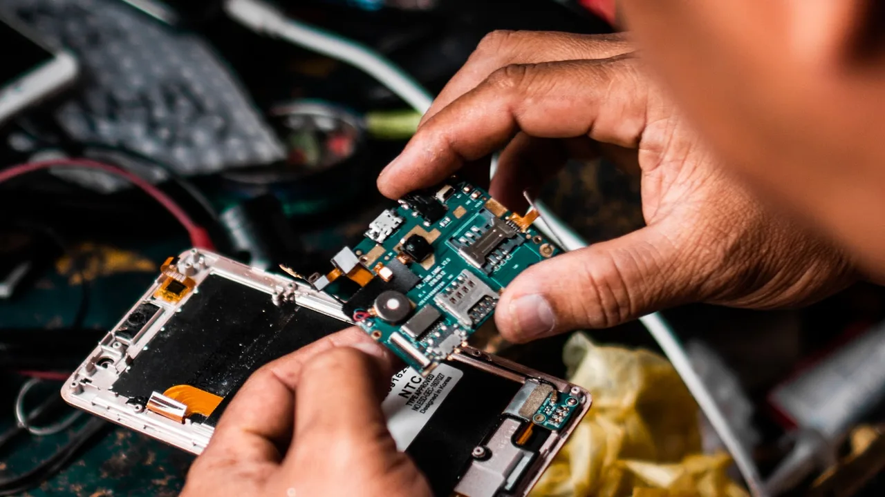 Technicien démontant la carte mère d'un smartphone sur l'établi d'un atelier de réparation